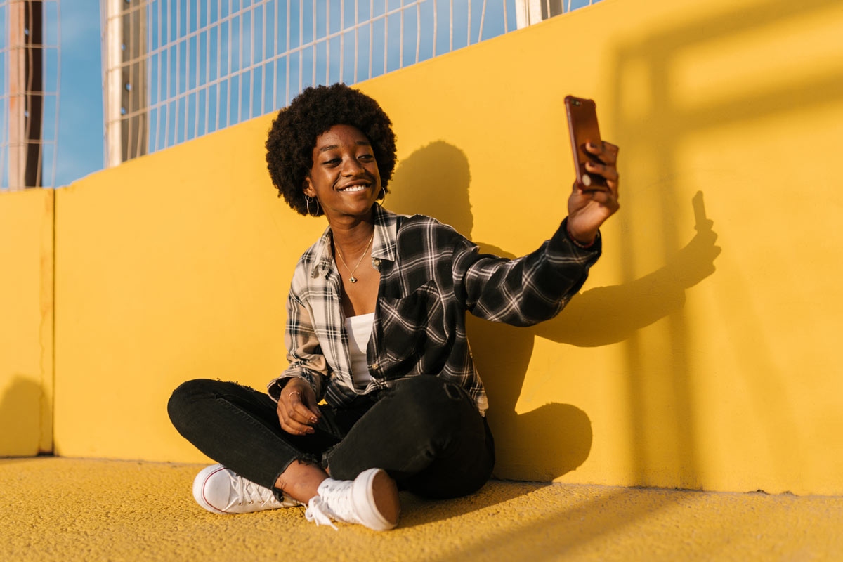 Girl sitting against yellow wall taking selfie