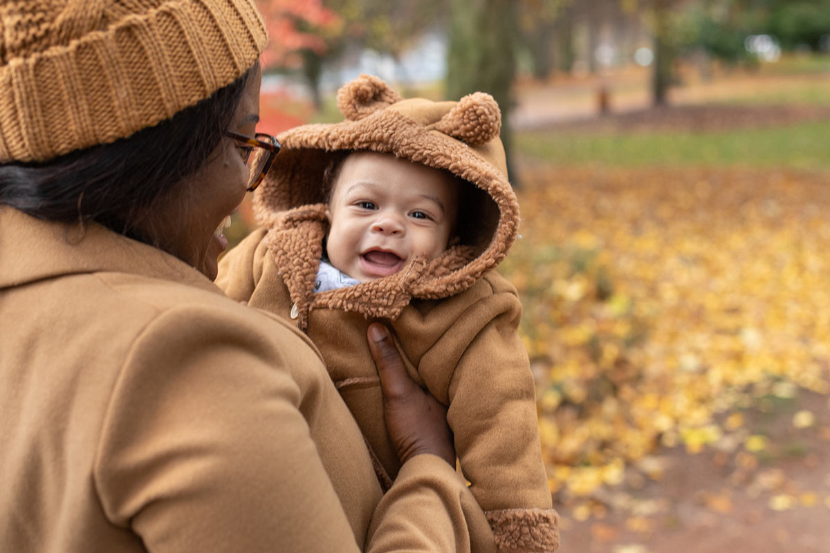 Mom holding small baby in autumn park wearing warm jacket with hood