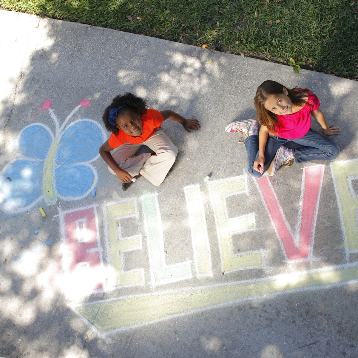 Girls writing believe on sidewalk