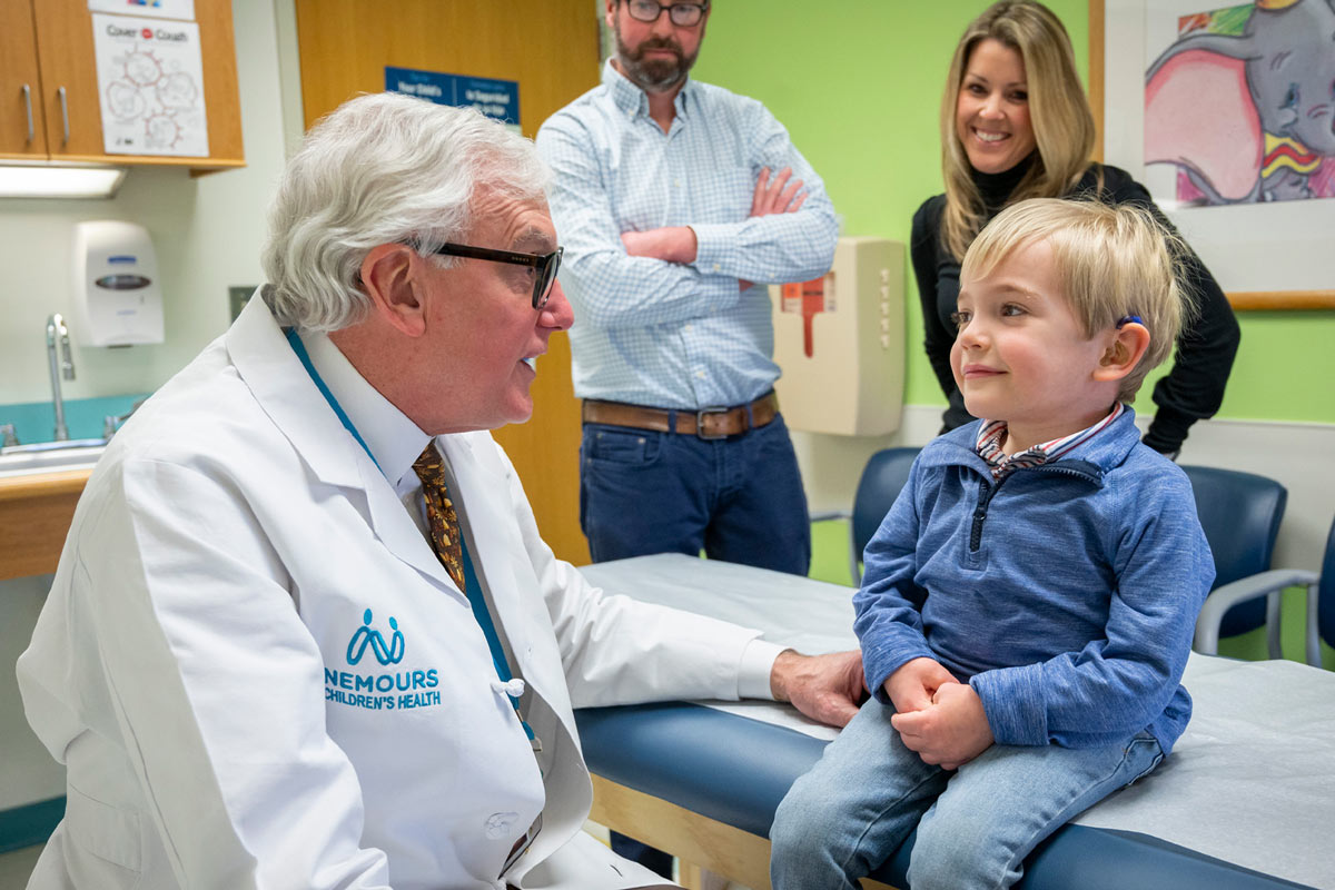 Doctor talking with little boy with parents in background