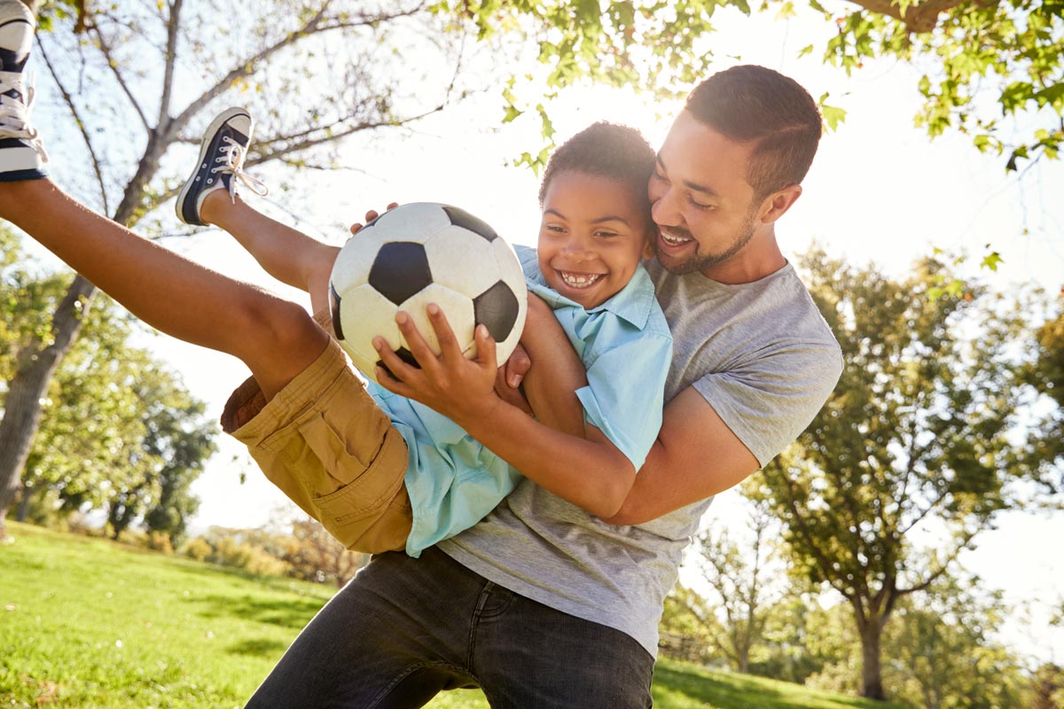father and son playing soccer in park