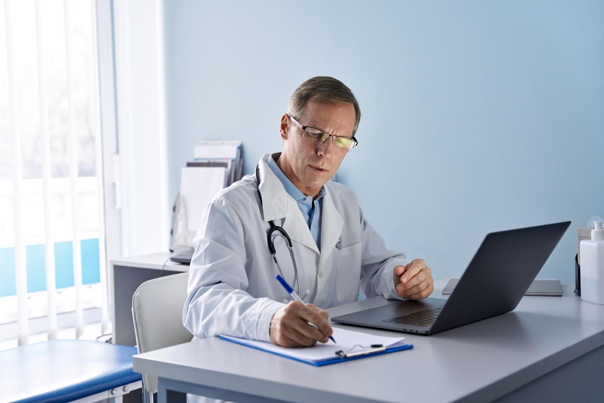 male doctor using laptop computer in hospital office writing healthcare report