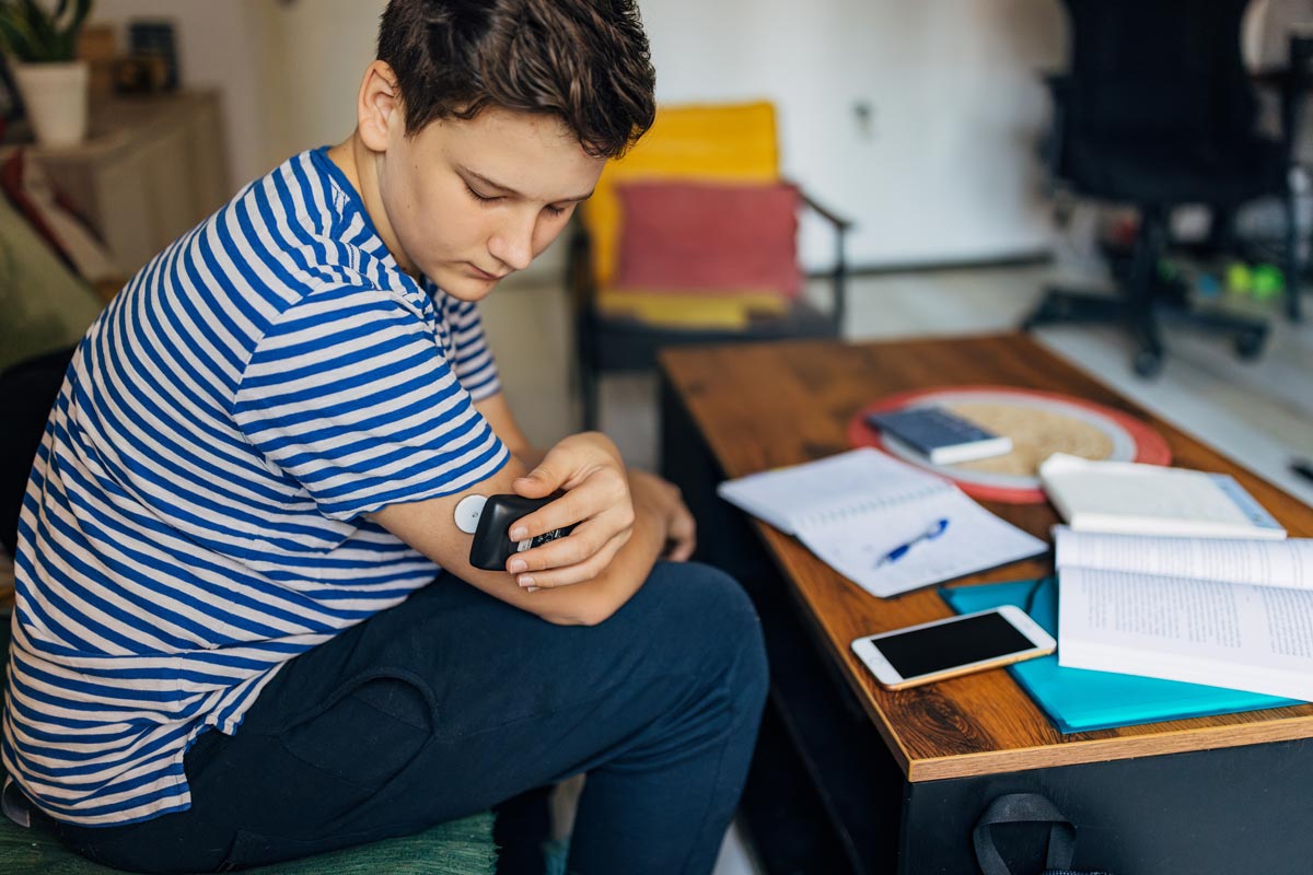 teenage boy using a continuous remote glucose monitor diabetes sensor at home