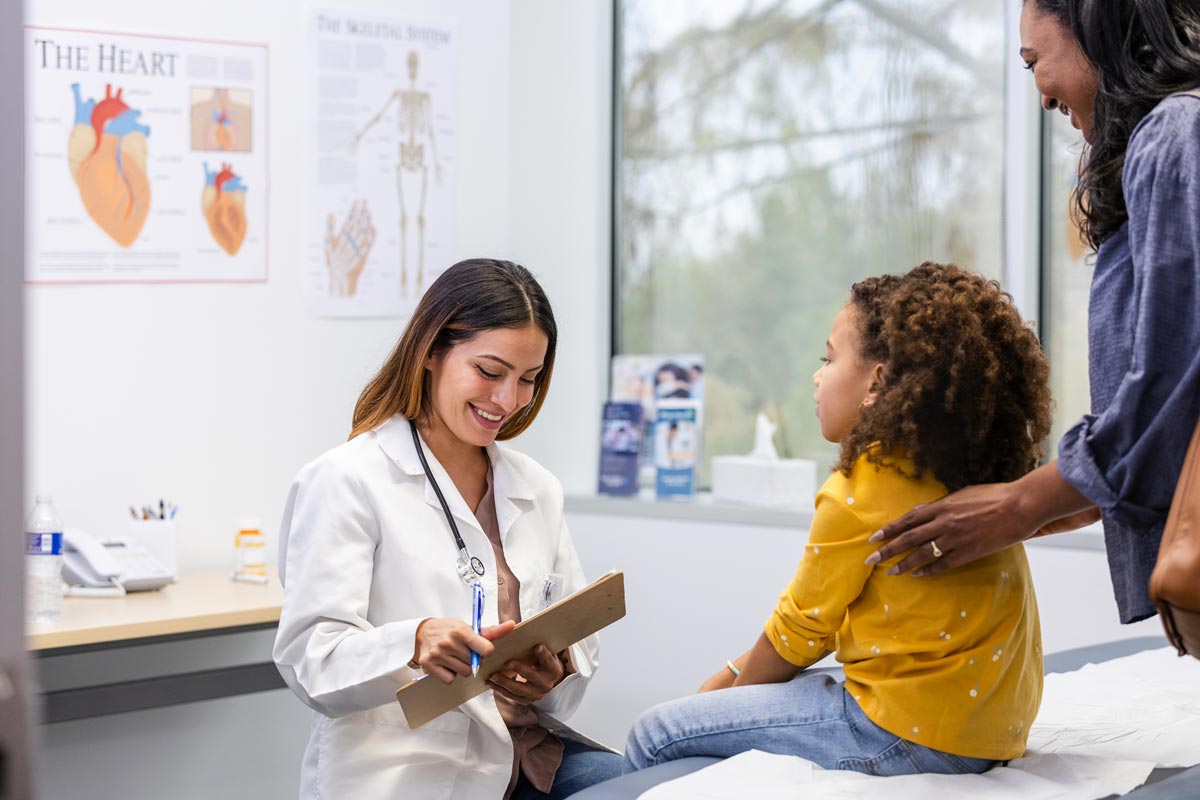 doctor smiles while listening to her young patient give her an update on her symptoms.