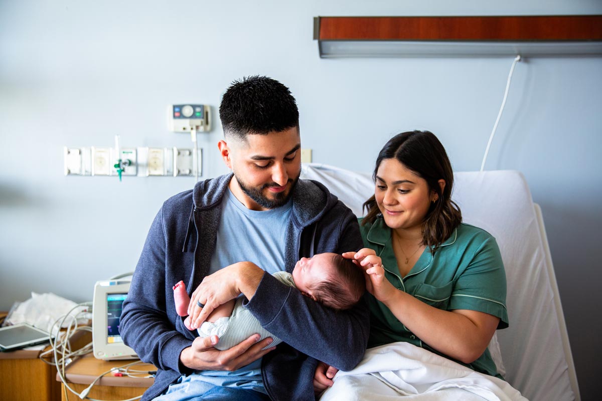 Young parents holding their newborn baby boy in the hospital bed